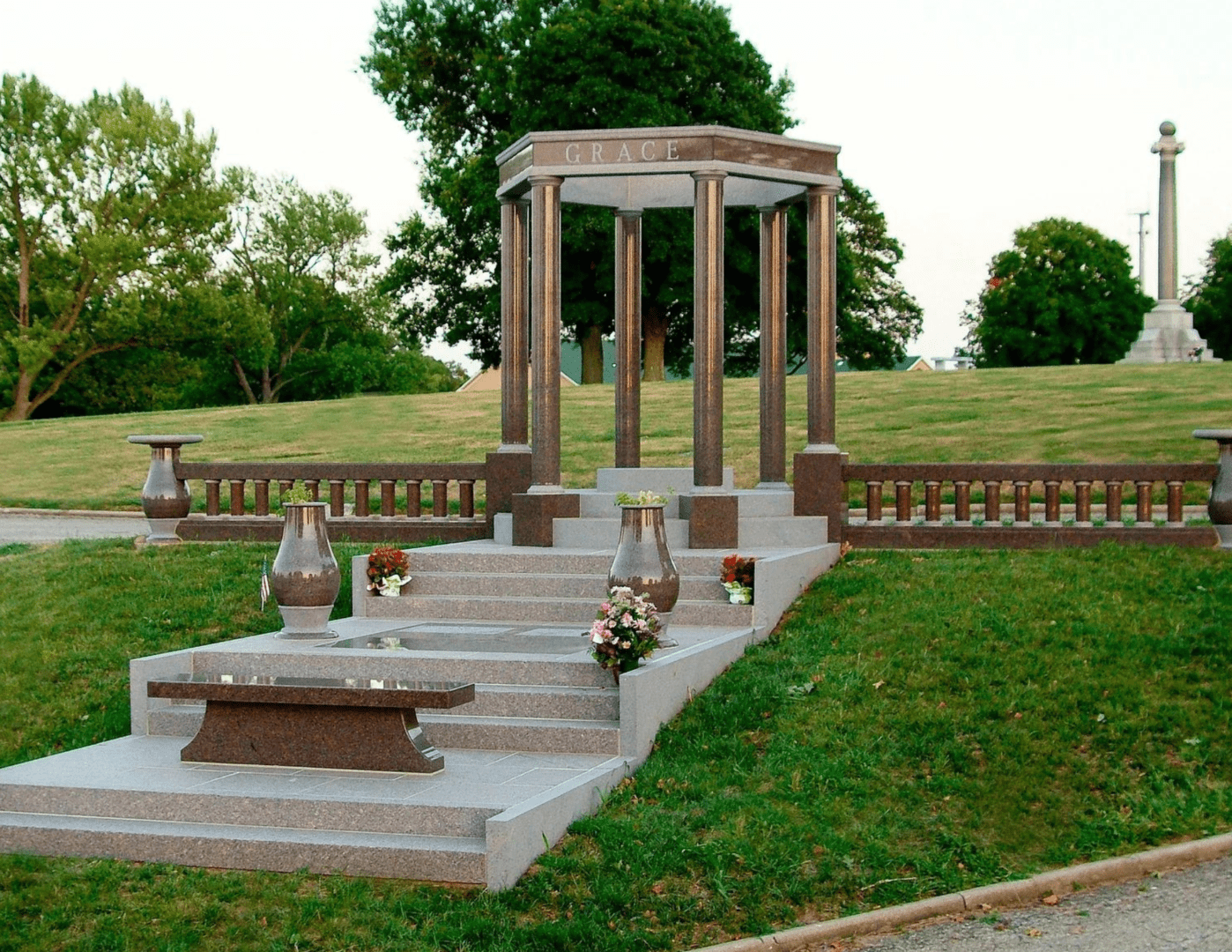 A stone bench sitting on top of grass near a gazebo.